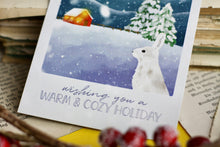 Lade das Bild in den Galerie-Viewer, Postkarte - Hase im Schnee - Polarlichter - Berglandschaft mit Hütte - warm and cozy holiday - Weihnachten Winter - Eigene Illustration