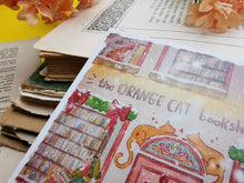 Lade das Bild in den Galerie-Viewer, Postkarte - Buchladen im Schnee - Weihnachten - orange cat bookshop - Aquarell - Cozy - Hund - Katze - Bücher - Eigene Illustration